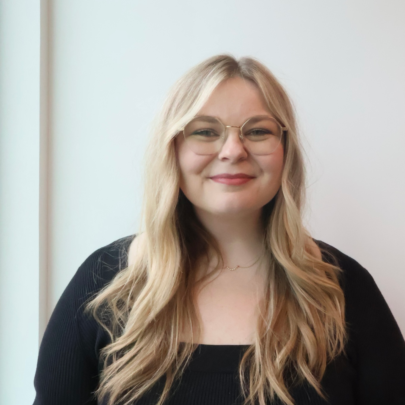 Staff member smiles at camera, wearing glasses with long blond hair.