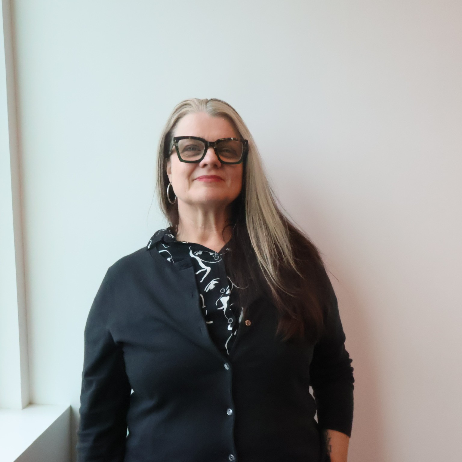 Staff member wearing black-rimmed glasses smiles into camera.